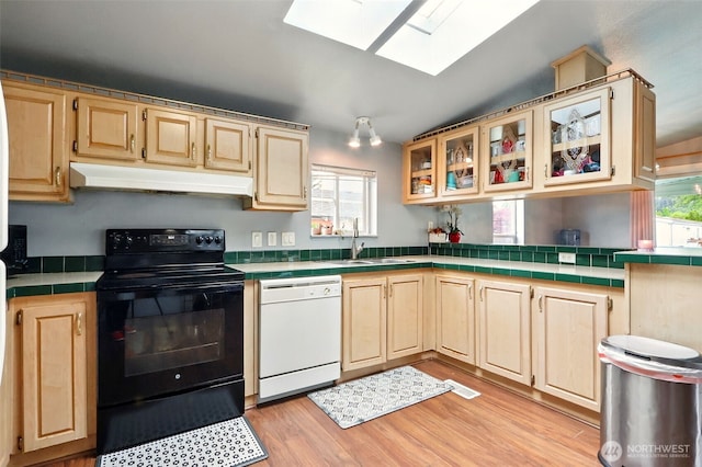 kitchen featuring white dishwasher, black range with electric stovetop, under cabinet range hood, tile countertops, and a skylight