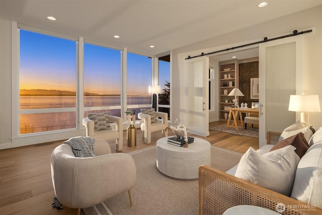 living room with a water view, wood finished floors, a barn door, baseboards, and recessed lighting