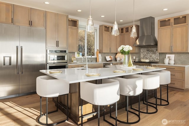 kitchen with a sink, stainless steel appliances, wall chimney range hood, a breakfast bar, and light wood-style flooring