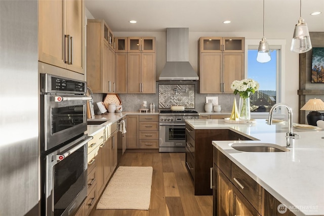 kitchen with stainless steel appliances, a sink, wall chimney exhaust hood, light countertops, and dark wood-style floors