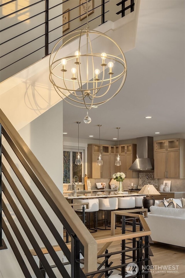 interior space featuring wall chimney range hood, a chandelier, wood finished floors, and backsplash
