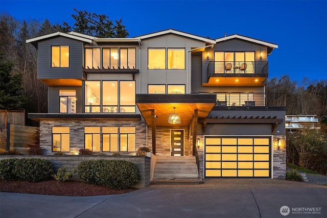 view of front of home with stone siding, driveway, an attached garage, and a balcony