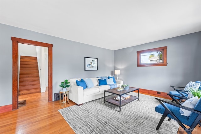 living room featuring stairway, light wood finished floors, and visible vents