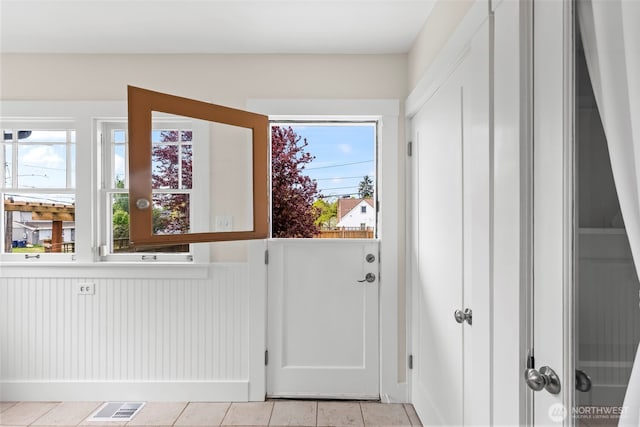 entryway featuring a wainscoted wall, light tile patterned floors, and visible vents