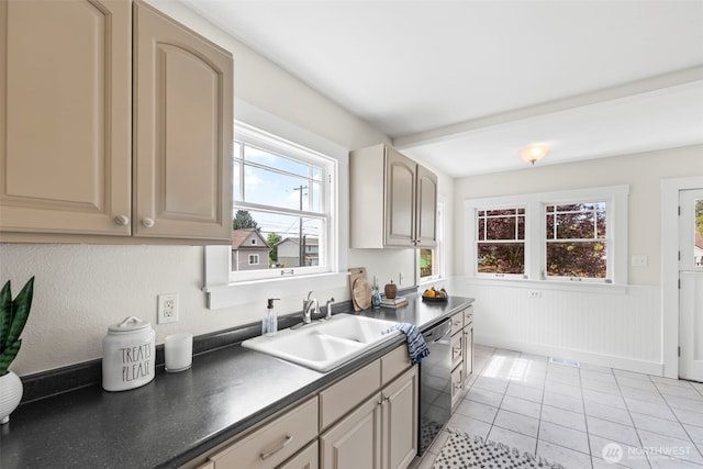 kitchen with light tile patterned floors, a sink, dark countertops, a wainscoted wall, and dishwasher