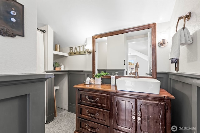 bathroom with a wainscoted wall, speckled floor, lofted ceiling, and vanity