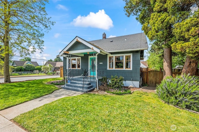 bungalow with a chimney, roof with shingles, a front lawn, and fence