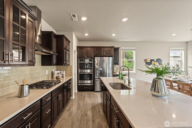 kitchen with appliances with stainless steel finishes, a sink, wall chimney exhaust hood, light countertops, and recessed lighting