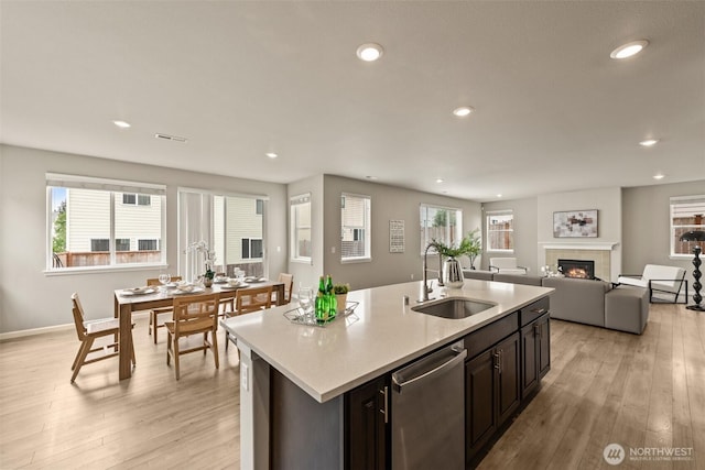 kitchen with a sink, stainless steel dishwasher, light countertops, light wood finished floors, and a tile fireplace