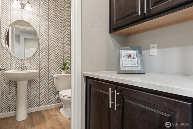 bathroom with wallpapered walls, toilet, wood finished floors, and a sink
