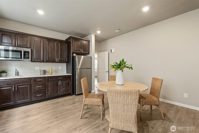 kitchen featuring appliances with stainless steel finishes, light wood-style flooring, dark brown cabinets, light countertops, and baseboards