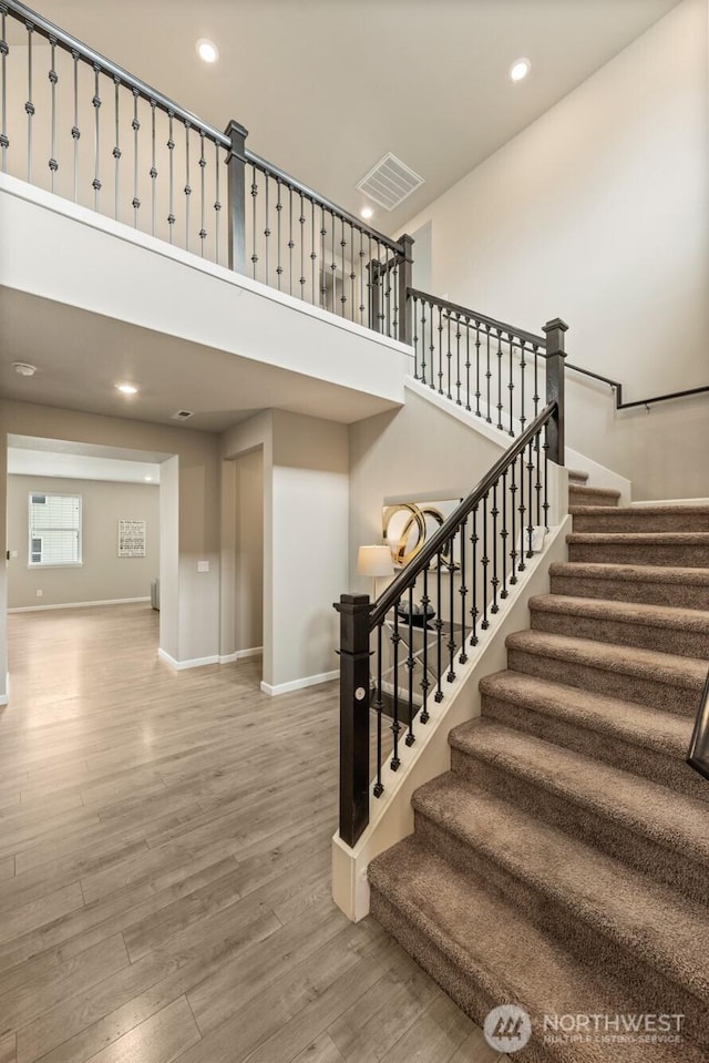 staircase featuring baseboards, wood finished floors, a high ceiling, and recessed lighting