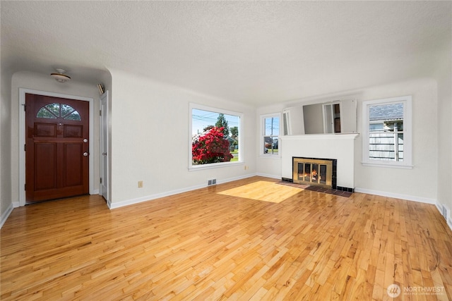 6027 S Bell St, Tacoma, WA 98408 - unfurnished living room with light wood-style flooring, baseboards, a tile fireplace, and a textured ceiling