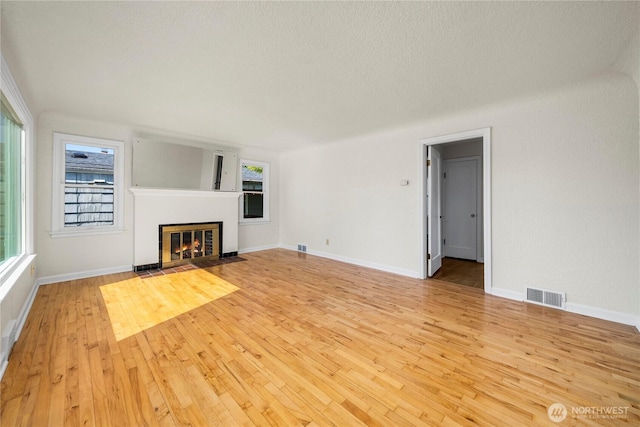 6027 S Bell St, Tacoma, WA 98408 - unfurnished living room featuring light wood-style flooring, plenty of natural light, a fireplace with flush hearth, and a textured ceiling