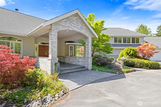 doorway to property with a shingled roof, stucco siding, and brick siding