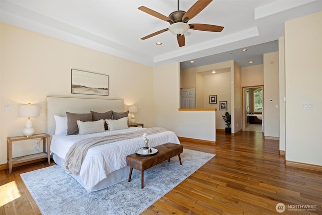 bedroom featuring baseboards, a raised ceiling, wood-type flooring, and recessed lighting