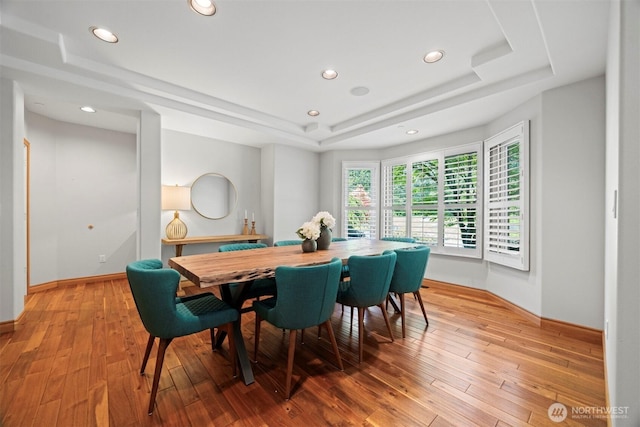 dining space featuring light wood finished floors, baseboards, a raised ceiling, and recessed lighting