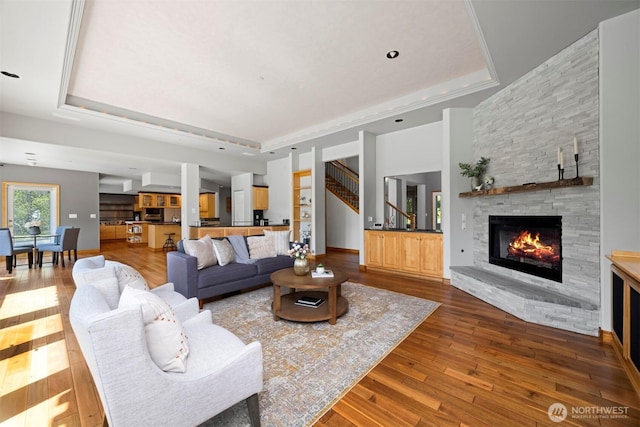 living area featuring a stone fireplace, a raised ceiling, and wood-type flooring