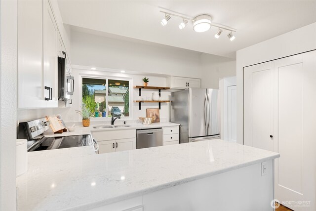 kitchen with appliances with stainless steel finishes, a sink, light stone counters, white cabinetry, and a peninsula