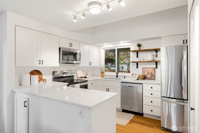 kitchen with stainless steel appliances, a sink, a peninsula, white cabinets, and light stone counters