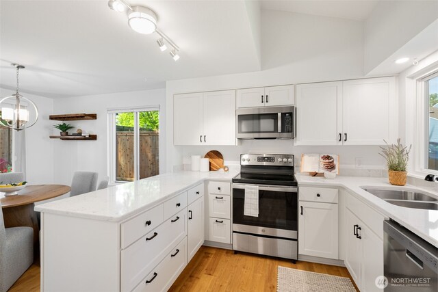 kitchen with stainless steel appliances, a sink, a peninsula, healthy amount of natural light, and vaulted ceiling