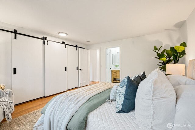 bedroom with a barn door, light wood-type flooring, and ensuite bath