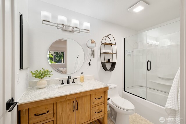 full bath featuring vanity, toilet, and bath / shower combo with glass door
