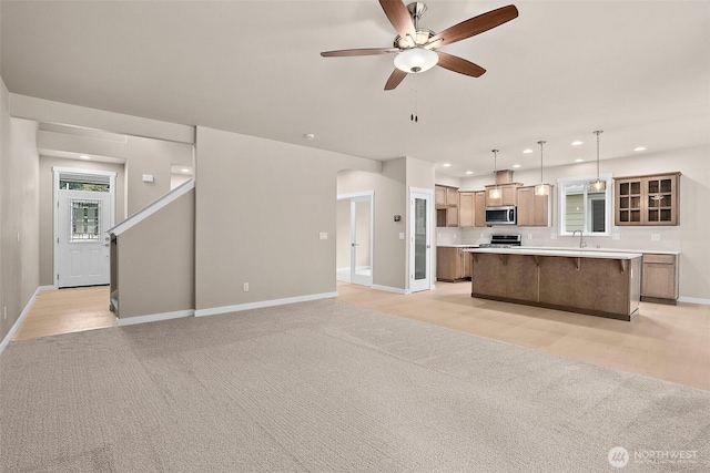 unfurnished living room with baseboards, arched walkways, recessed lighting, light colored carpet, and ceiling fan