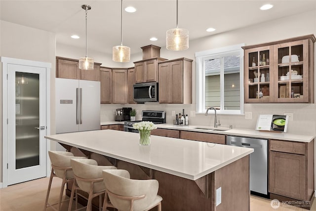 kitchen with appliances with stainless steel finishes, a sink, a center island, a kitchen bar, and decorative light fixtures