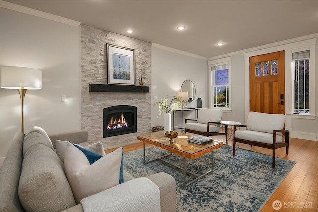 living room featuring hardwood / wood-style flooring, ornamental molding, a stone fireplace, and recessed lighting