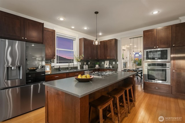 kitchen with appliances with stainless steel finishes, a sink, dark countertops, a breakfast bar area, and ornamental molding