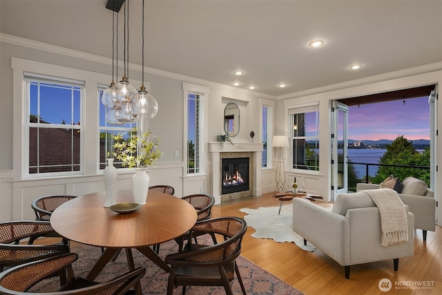 dining space featuring ornamental molding, a decorative wall, light wood-type flooring, a high end fireplace, and recessed lighting