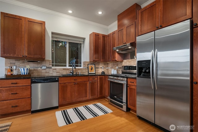 kitchen featuring stainless steel appliances, under cabinet range hood, a sink, crown molding, and decorative backsplash