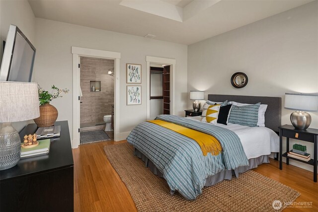 bedroom with wood finished floors, ensuite bath, and a walk in closet