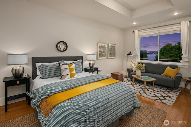 bedroom with wood finished floors, recessed lighting, baseboards, and a raised ceiling