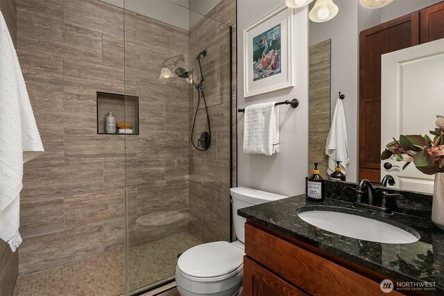 bathroom with toilet, tiled shower, and vanity