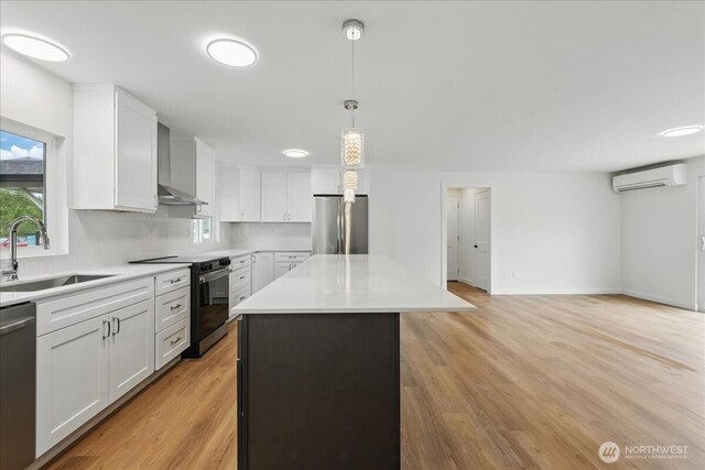 kitchen featuring appliances with stainless steel finishes, a sink, wall chimney exhaust hood, a wall mounted air conditioner, and a kitchen island