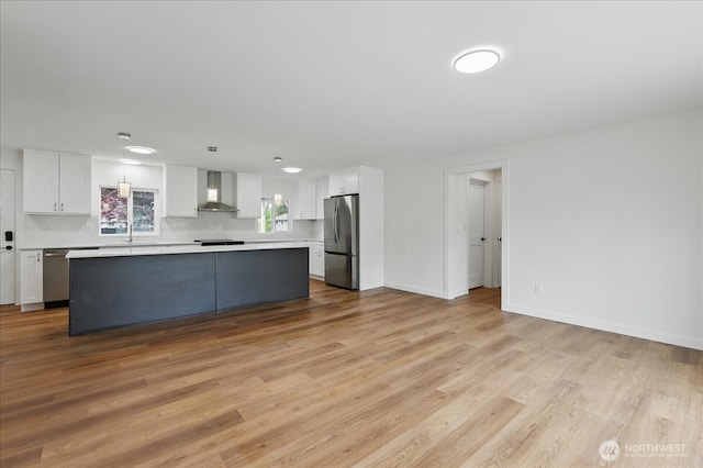 kitchen with stainless steel appliances, wall chimney exhaust hood, white cabinetry, light countertops, and a kitchen island