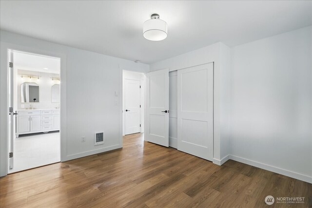unfurnished bedroom with wood finished floors, baseboards, a closet, a sink, and connected bathroom