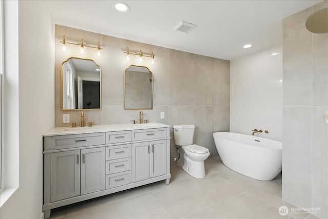 bathroom featuring tile walls, a freestanding bath, double vanity, tile patterned floors, and toilet