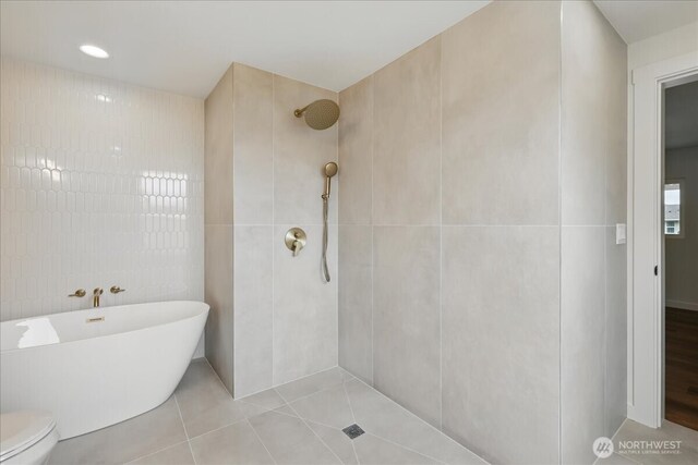 bathroom with tile walls, a tile shower, tile patterned flooring, a freestanding tub, and toilet
