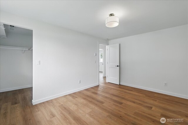 unfurnished bedroom featuring wood finished floors, baseboards, a closet, and a spacious closet
