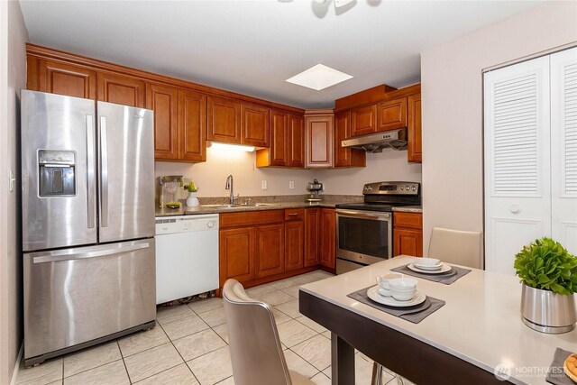 kitchen with under cabinet range hood, light tile patterned floors, a sink, brown cabinets, and appliances with stainless steel finishes