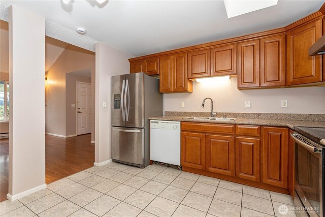 kitchen featuring light stone countertops, brown cabinetry, light tile patterned floors, a sink, and stainless steel appliances