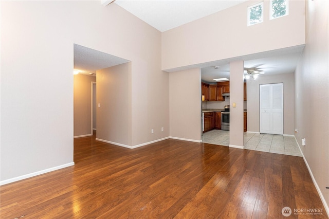 unfurnished living room featuring light wood finished floors, a high ceiling, baseboards, and ceiling fan