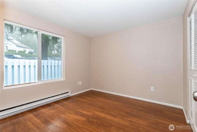 spare room with a baseboard radiator, baseboards, and dark wood finished floors