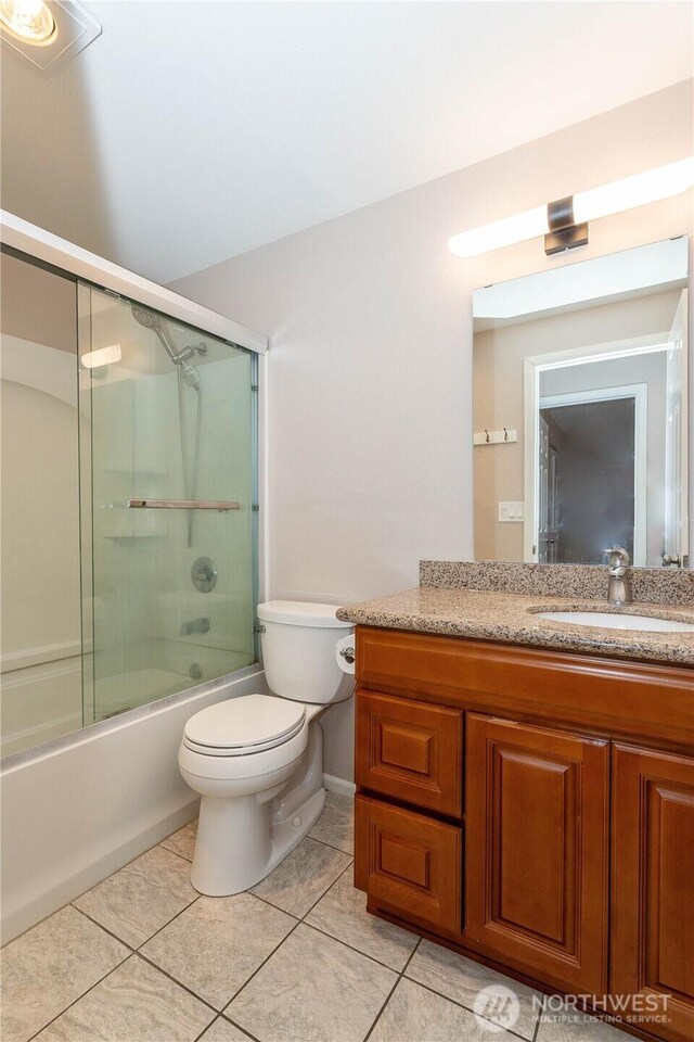 full bath featuring toilet, vanity, tile patterned flooring, bath / shower combo with glass door, and baseboards