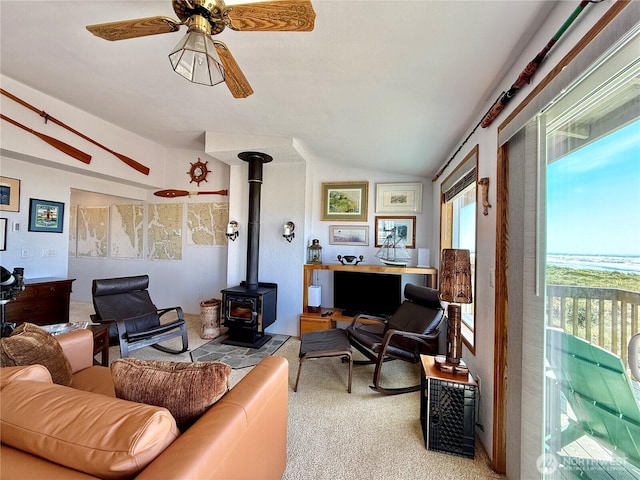 living area featuring lofted ceiling, a wood stove, ceiling fan, and carpet