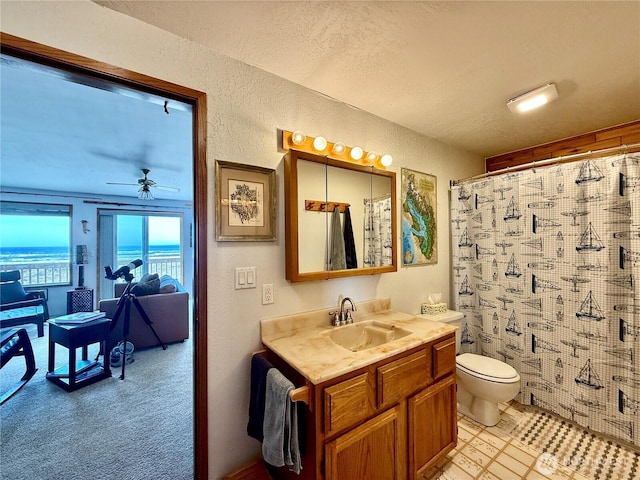 full bath featuring toilet, vanity, ceiling fan, and a textured wall