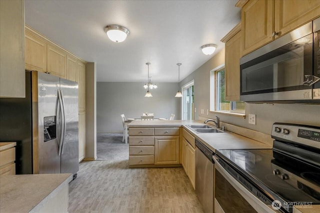 kitchen with a sink, a peninsula, stainless steel appliances, light countertops, and light brown cabinets